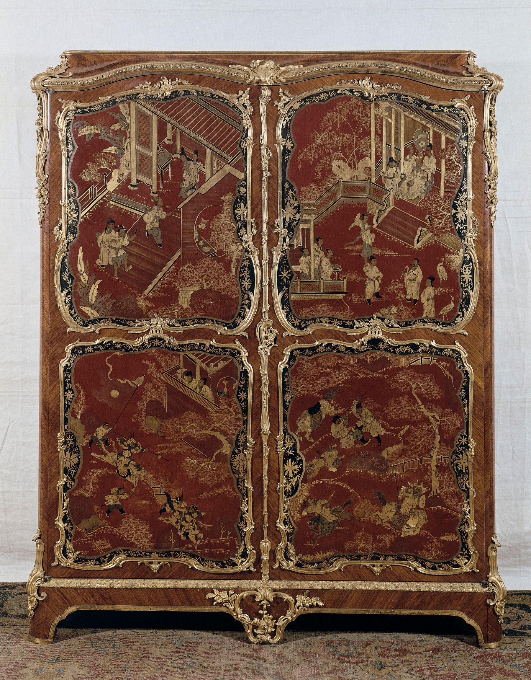 “a large armoire with four red lacquer panels featuring Chinese figures and framed with floral gilt bronze molding”