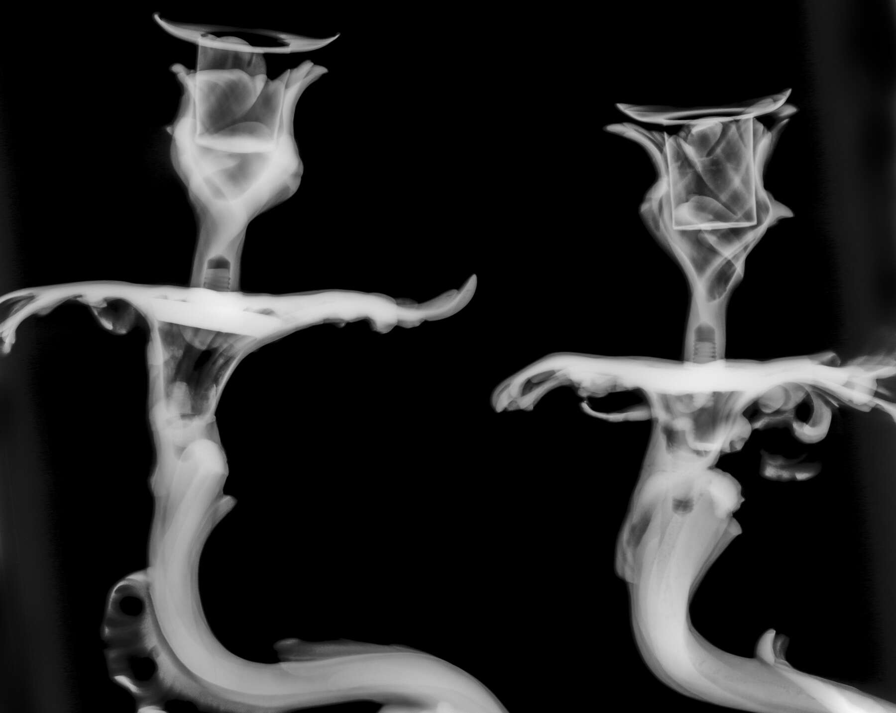 black-and-white x-ray of the gilt bronze candlestick mounts, revealing the threaded metal rods that connect the candle-holders to the bases