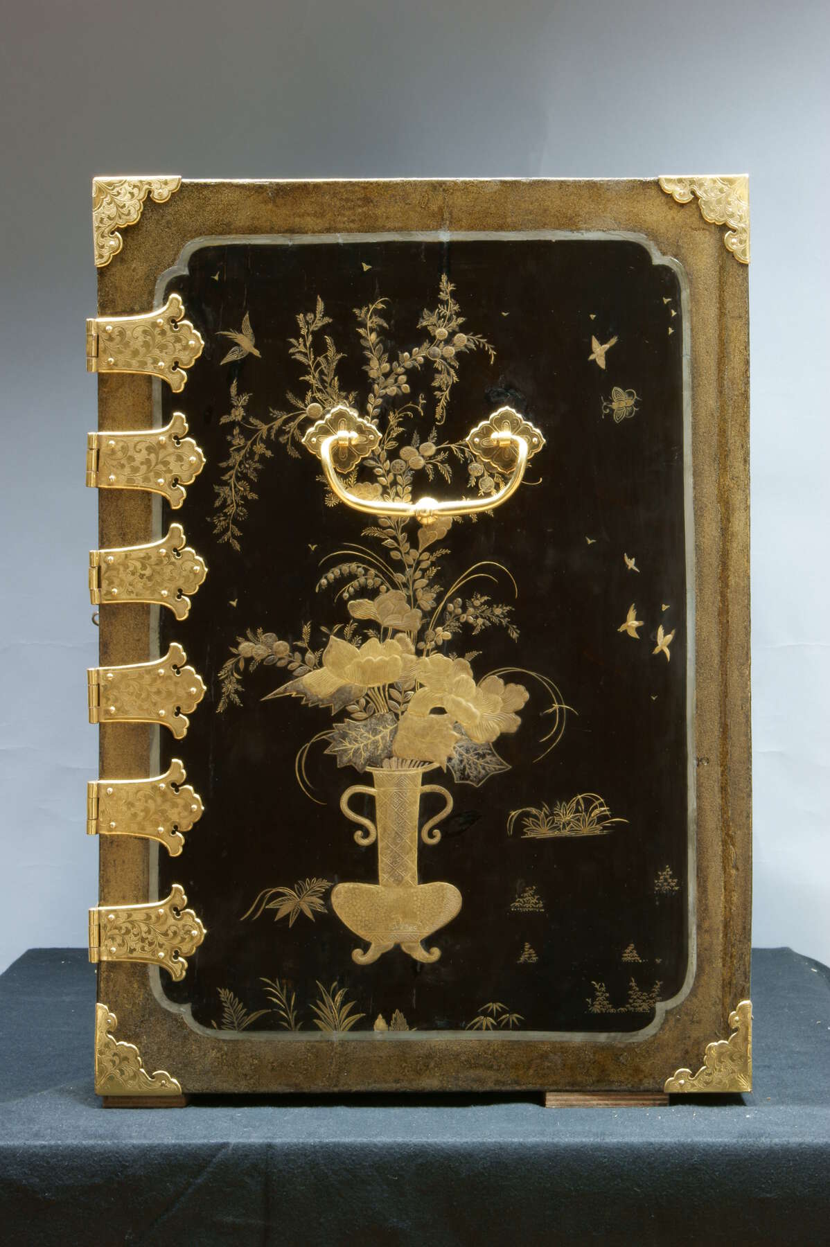 frontal view of the side panel of an additional lacquer cabinet, revealing black and gold lacquer designs of a vase of flowers, birds, and various foliage in a similar design to the side panels of the commode