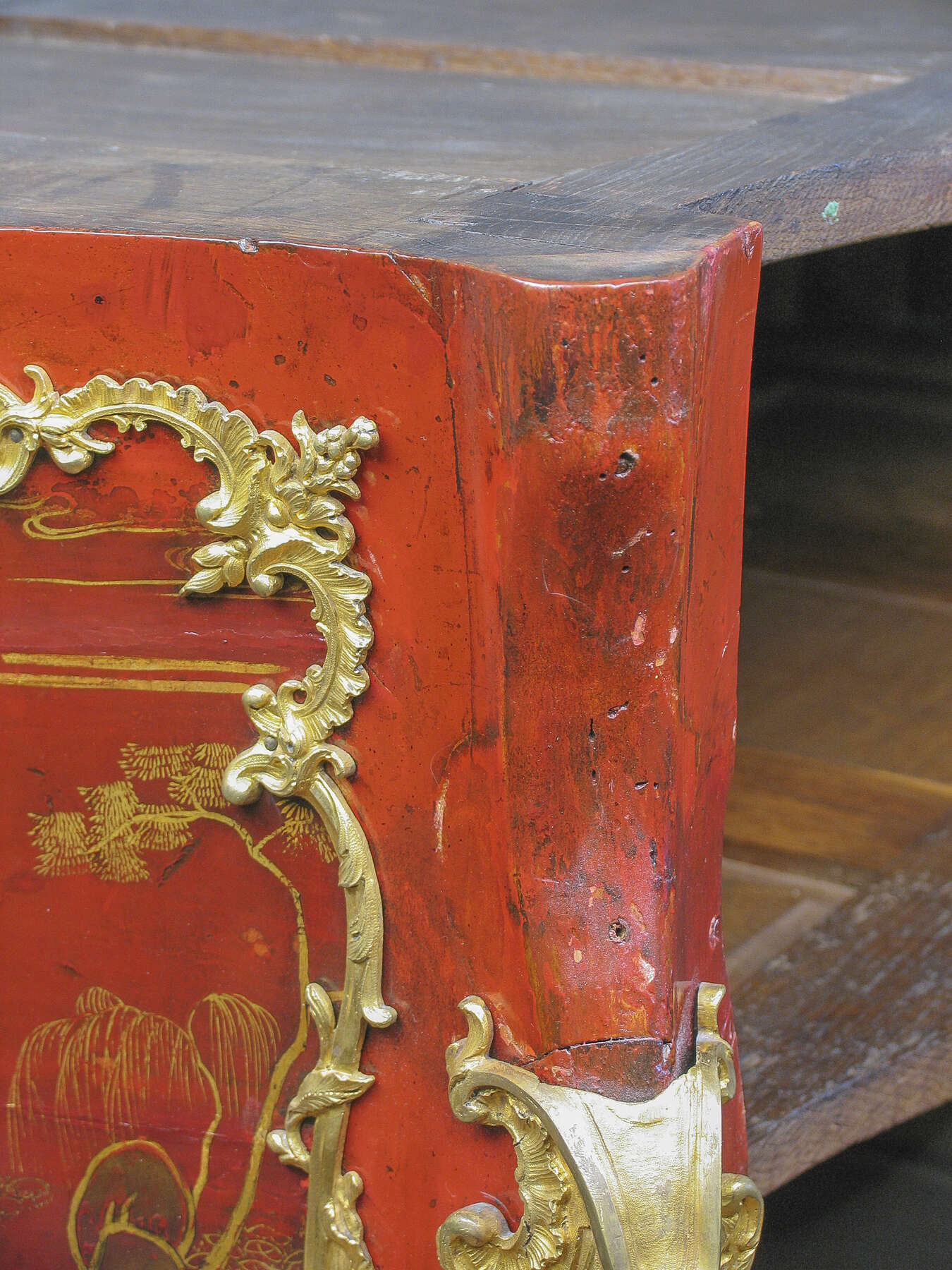 detail of one of the commode’s corners, with a horizontal strip of wood visible at the top of the bright reddish-orange leg
