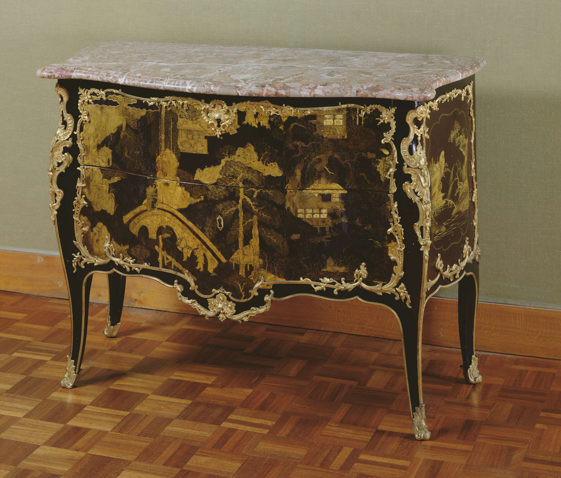 three-quarter view of a black commode decorated with gilt bronze mounts, lacquer designs with gold, and a light pink and white speckled marble top