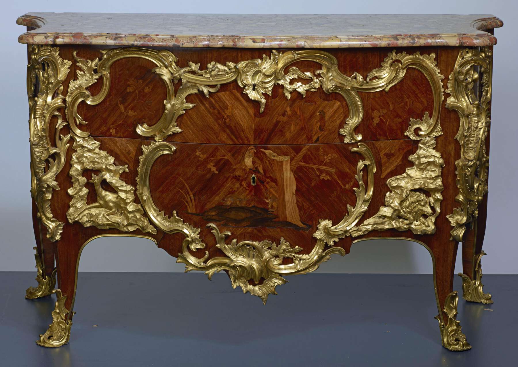 frontal view of an additional example of a paired commode, featuring marquetry of birds perched in a tree and gilt bronze mounts, similar to the Getty pair